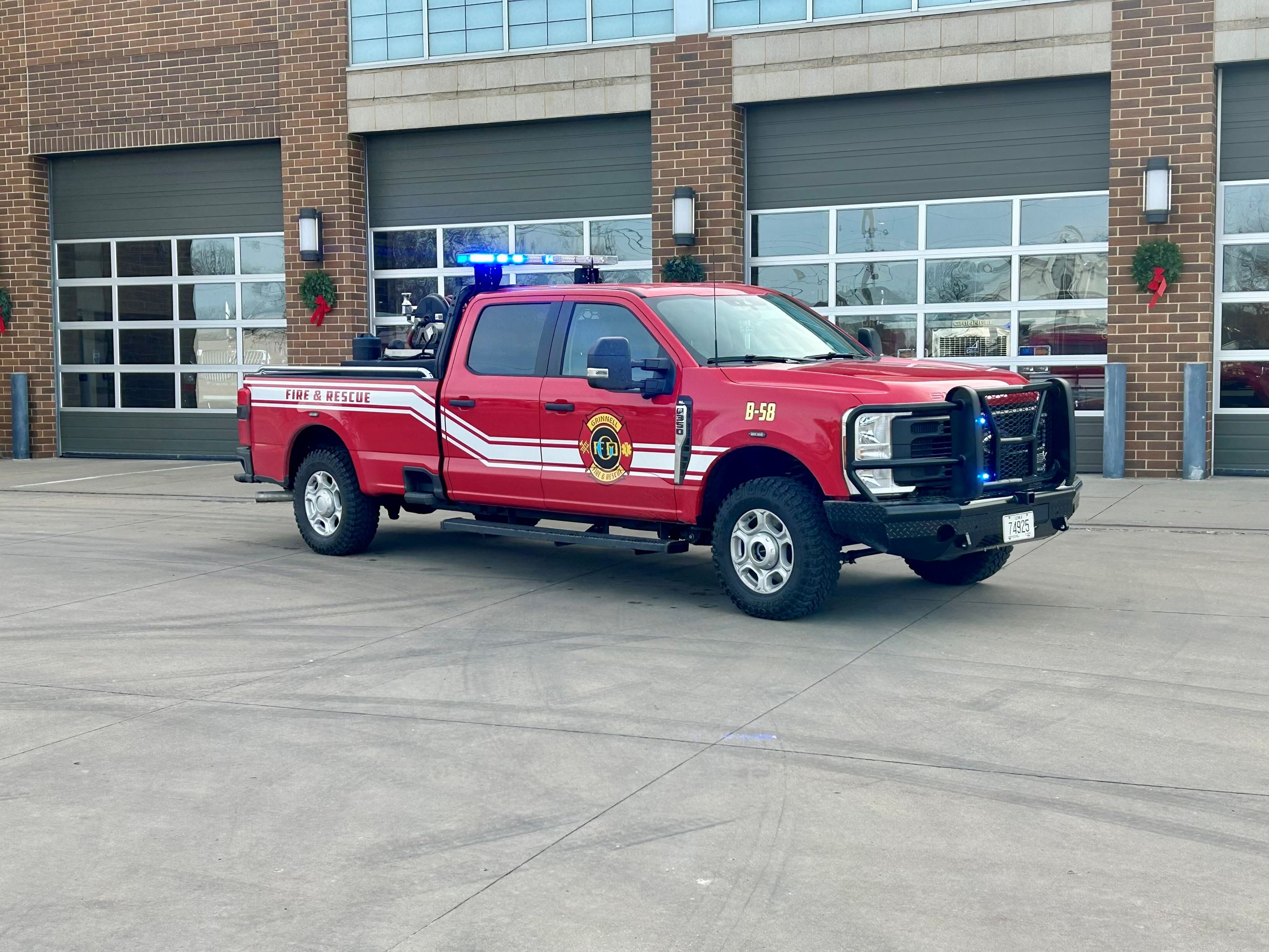 A red 4 door pickup truck with flashing blue lights and Grinnell Fire and Rescue decals