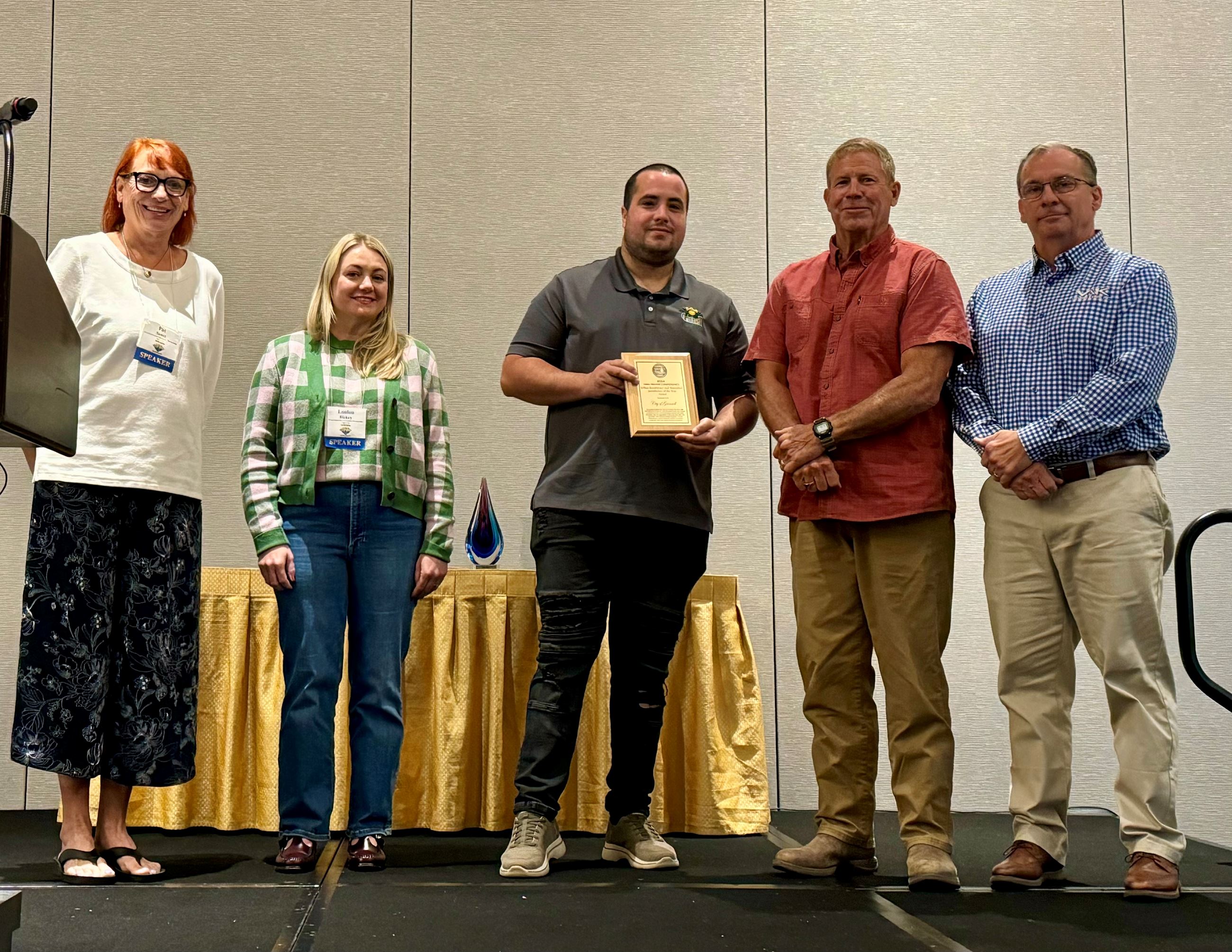 Five people on stage (2 from ISWEP and 3 from the City of Grinnell) holding an award plaque